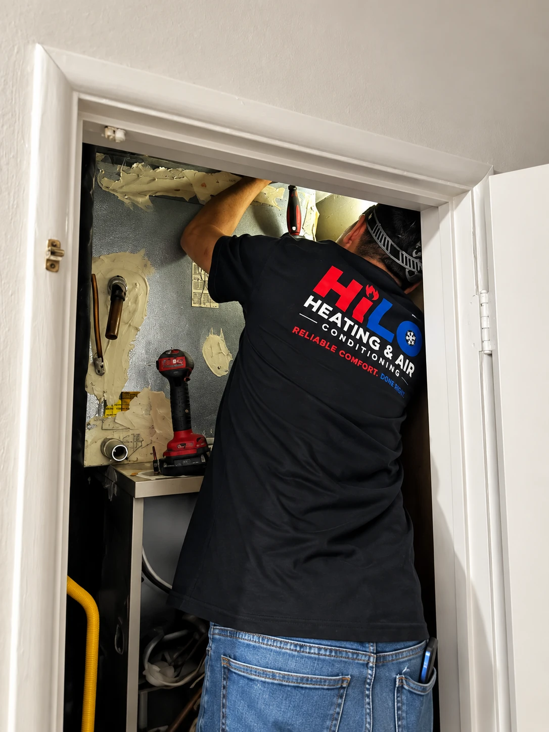 HiLo Heating & Air technician servicing an indoor air handler in a residential closet